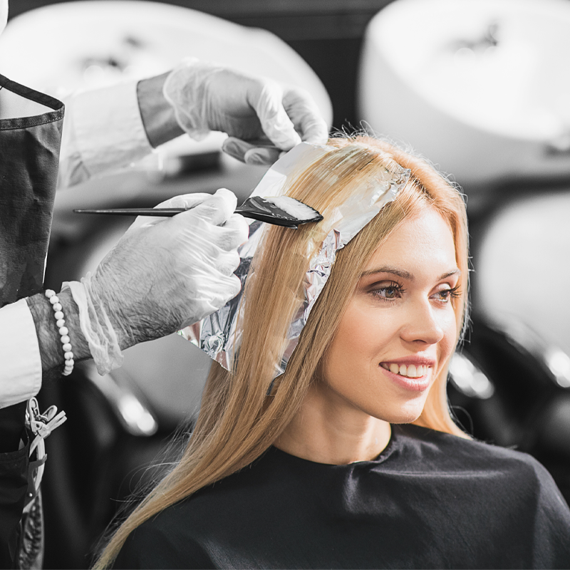 ragazza bionda che fa una tinta ai capelli. Colorista al lavoro su una tecnica di colore specializzata in salone.